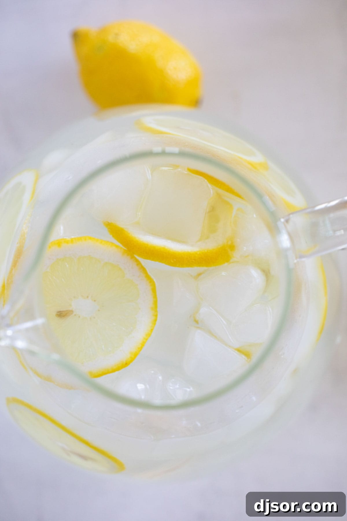 Sweet Lemon Refreshment 5 A clear pitcher filled with crystal-clear sweet lemon water, glistening with ice and garnished with fresh lemon slices.