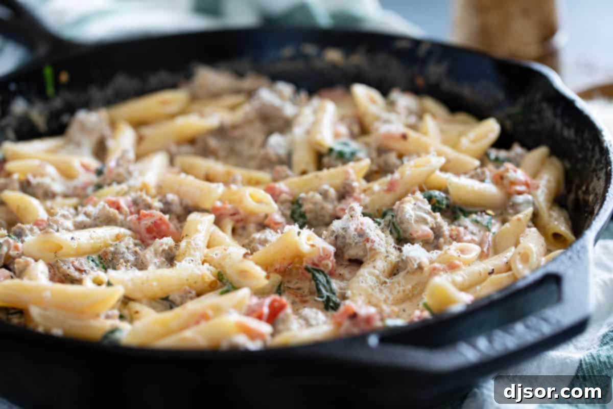 Skillet filled with Tuscan pasta with sausage topped with parmesan cheese.