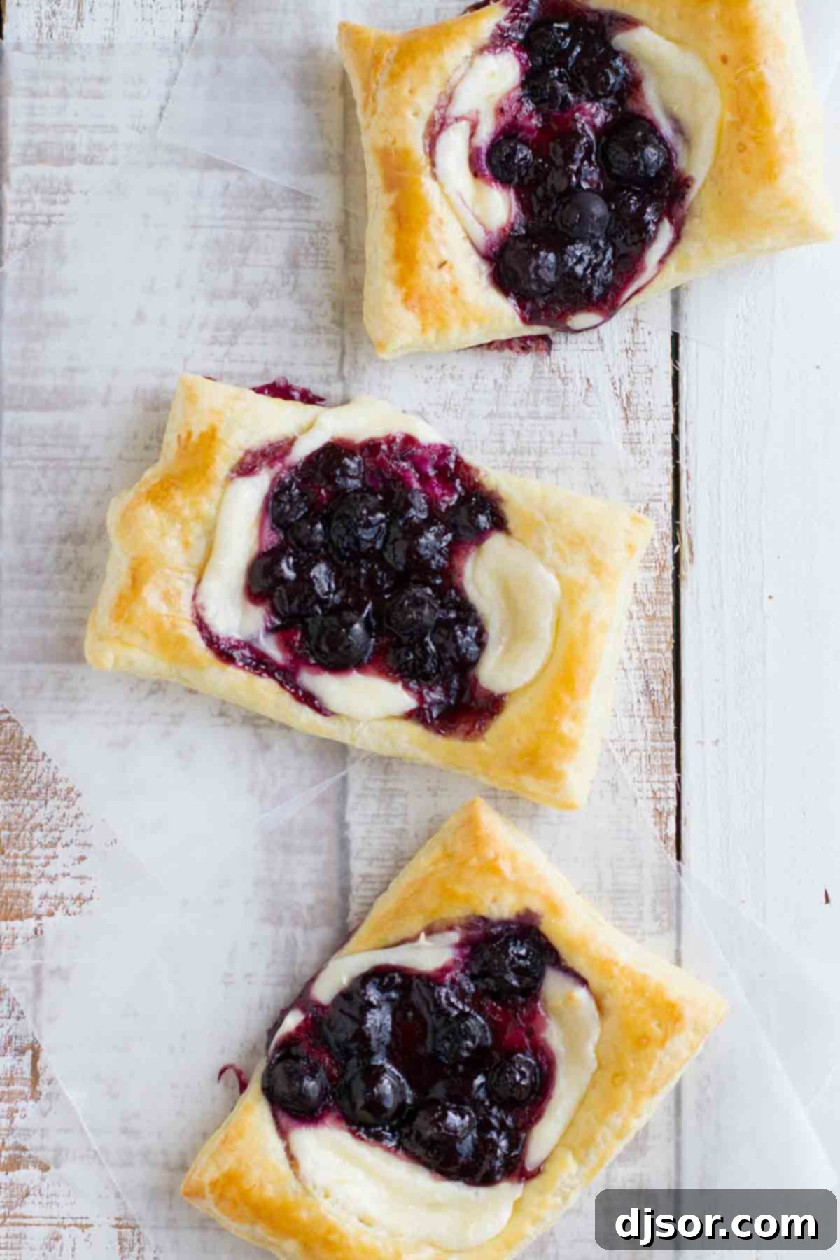 Close-up top view of a single puff pastry danish, showcasing the golden-brown crust, creamy cheese, and vibrant blueberries.
