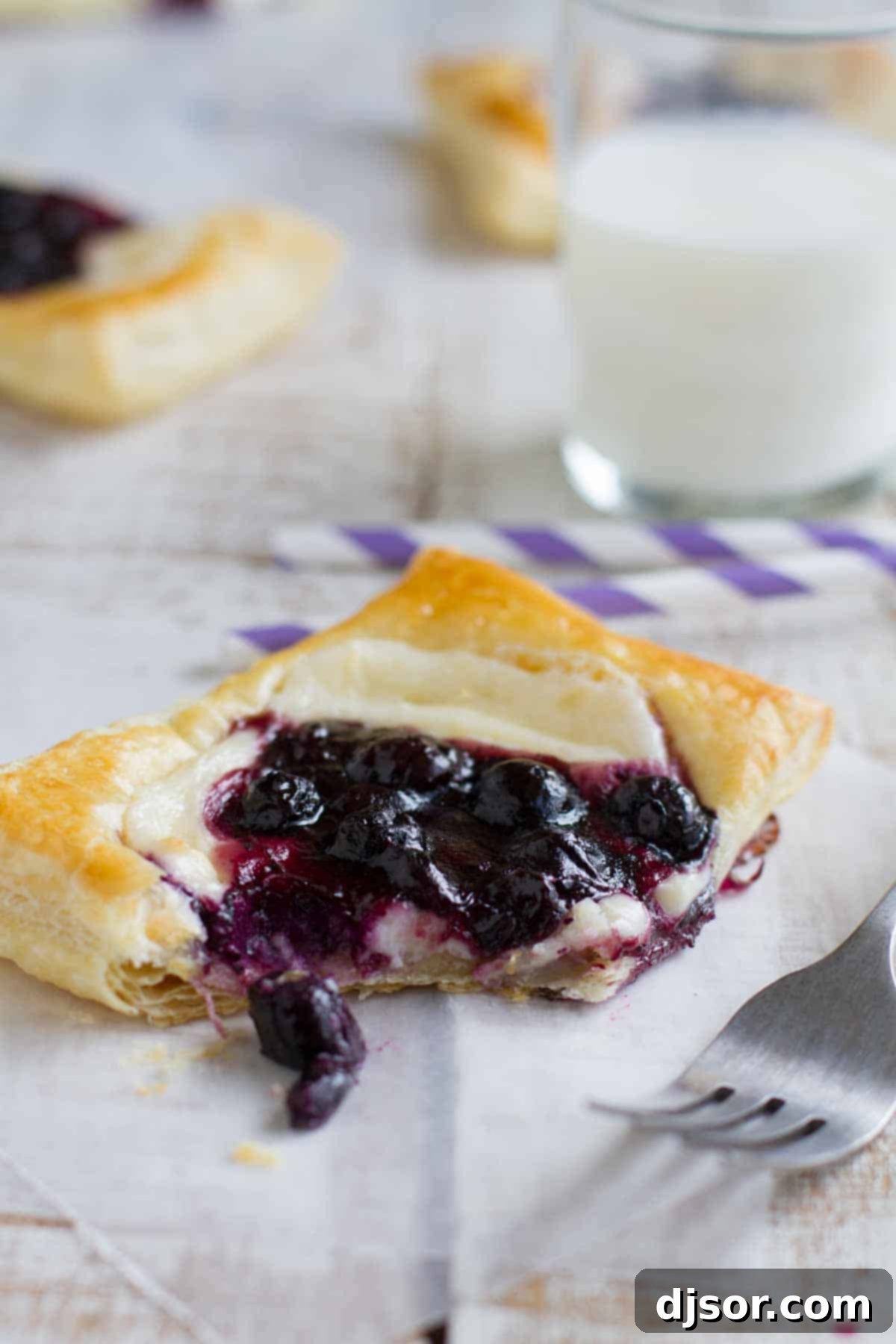 A stack of golden-brown puff pastry danishes with blueberry and cream cheese filling, dusted with powdered sugar.