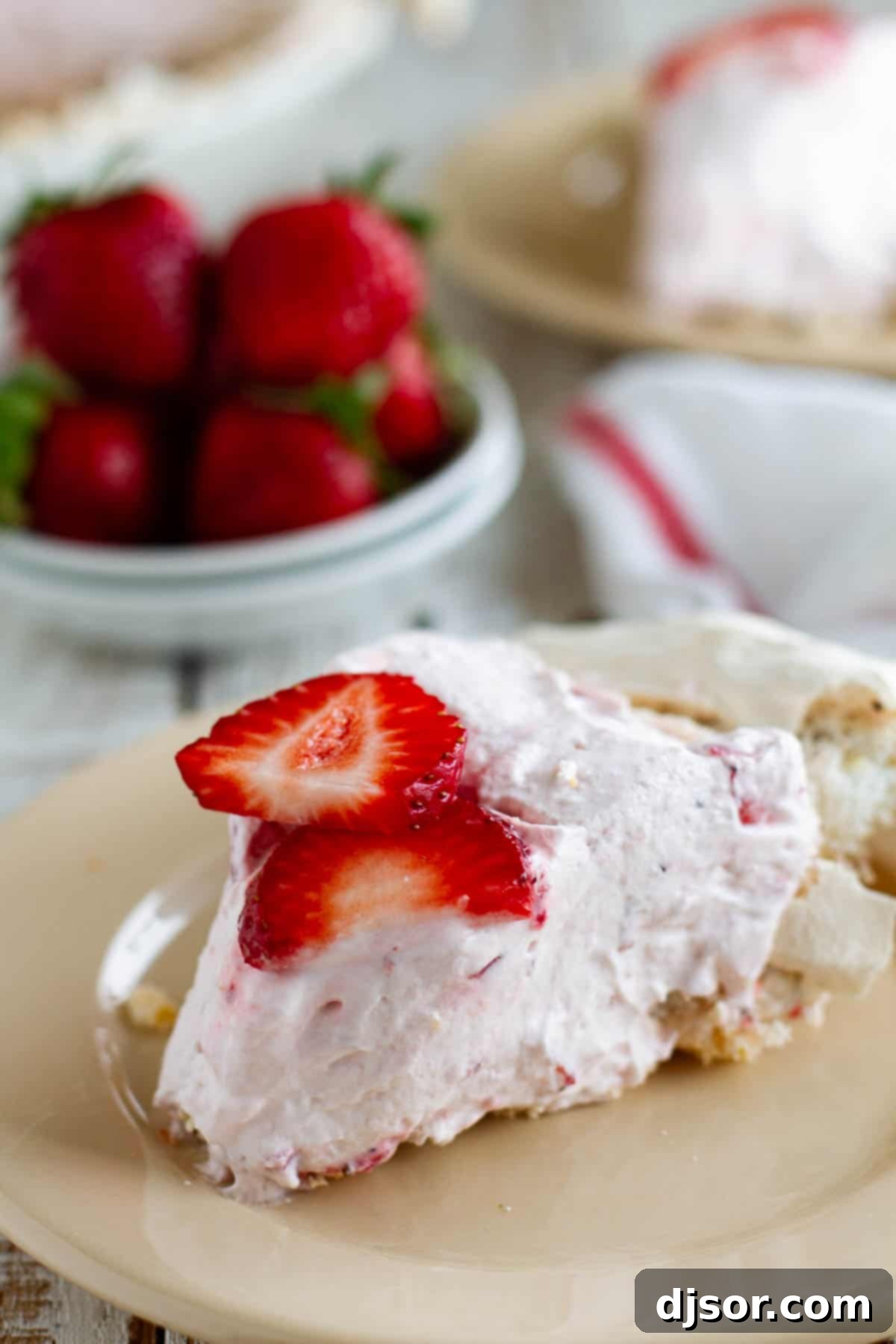 Strawberry Cream Angel Pie Slice A perfectly sliced piece of Strawberry Cream Angel Pie on a white plate, showcasing its ethereal meringue crust and rich pink strawberry filling, topped with a fresh strawberry. The crust is visibly crisp with pecan pieces.
