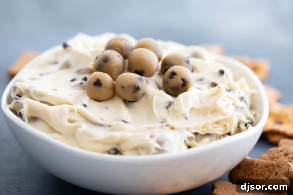 This Chocolate Chip Cookie Dough Dip is a sweet cream cheese dip that is loaded with balls of egg-free cookie dough. Serve with graham crackers, vanilla wafers, or pretzel crisps. bowl of Chocolate Chip Cookie Dough Dip with cookie dough balls on top