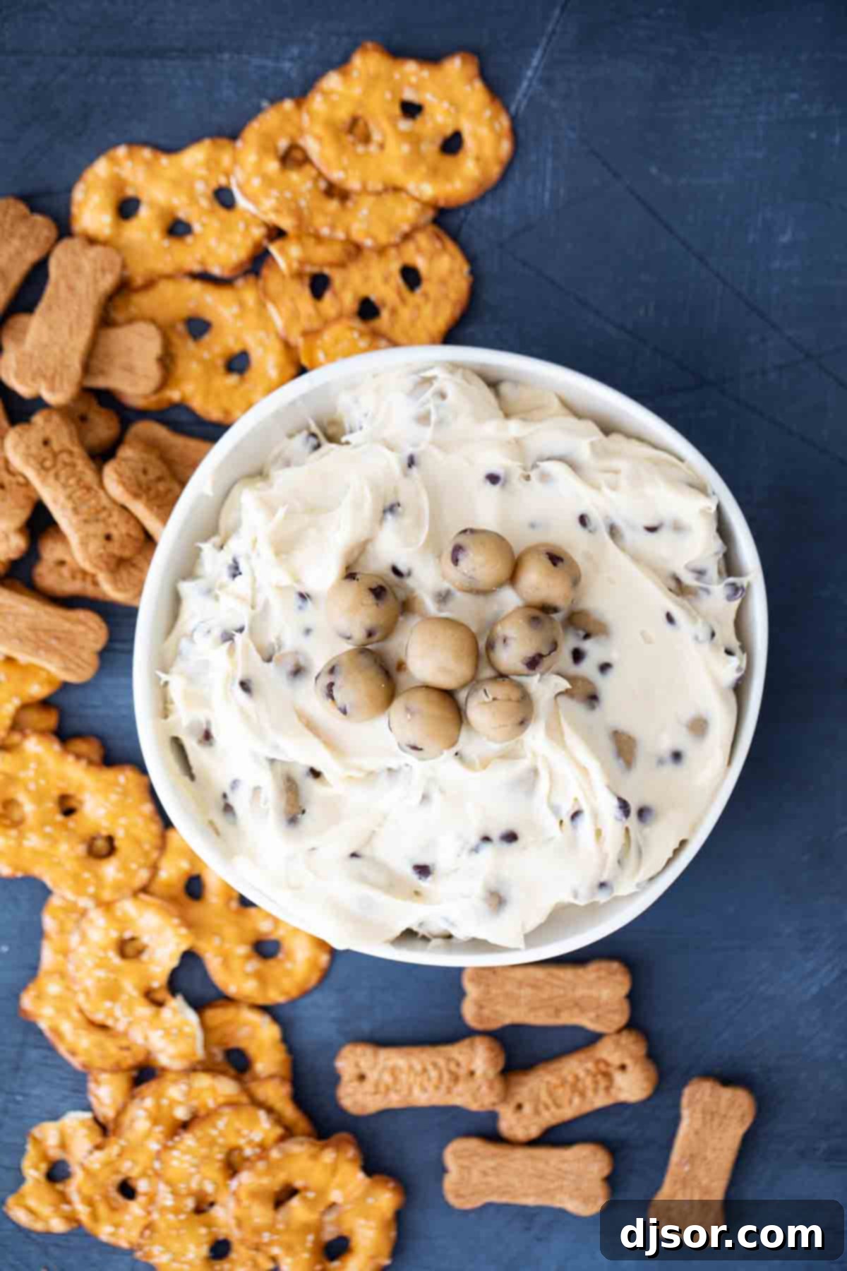 This Chocolate Chip Cookie Dough Dip is a sweet cream cheese dip that is loaded with balls of egg-free cookie dough. Serve with graham crackers, vanilla wafers, or pretzel crisps. overhead view of chocolate chip cookie dough dip with pretzel crisps and graham crackers
