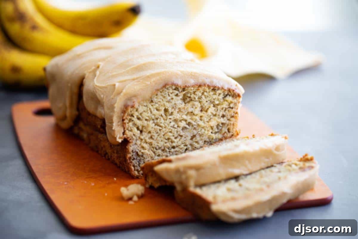 A perfectly sliced loaf of banana bread revealing its moist interior, generously topped with glistening caramel icing.