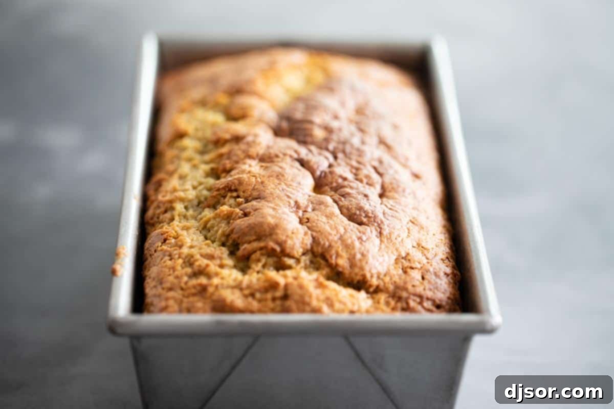 Freshly baked banana bread cooling in a loaf pan, ready for its caramel topping, highlighting its golden-brown crust.