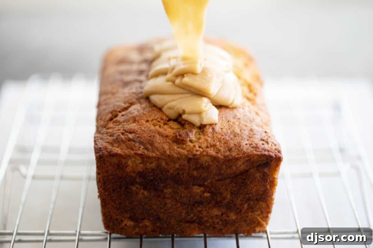 Rich caramel icing being poured generously over a golden-brown loaf of banana bread, creating a beautiful glaze.