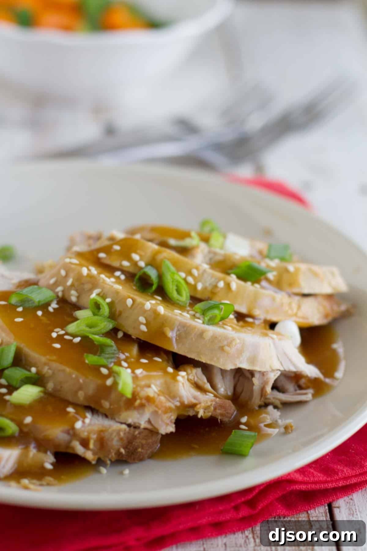 Plate with slices of sesame pork roast that are topped with a simple sauce and sesame seeds.