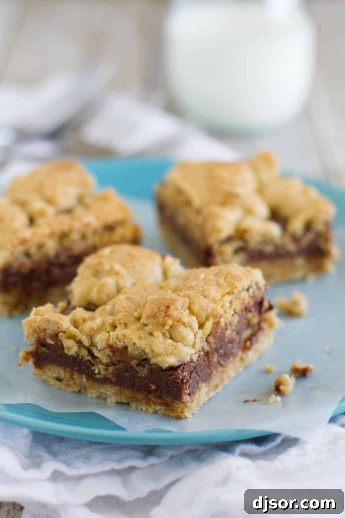 Gooey chocolate is sandwiched between two layers of oatmeal cookies in these decadent Oatmeal Fudge Bars. Three Oatmeal Fudge Bars on a plate with parchment under them, showcasing their rich layers.