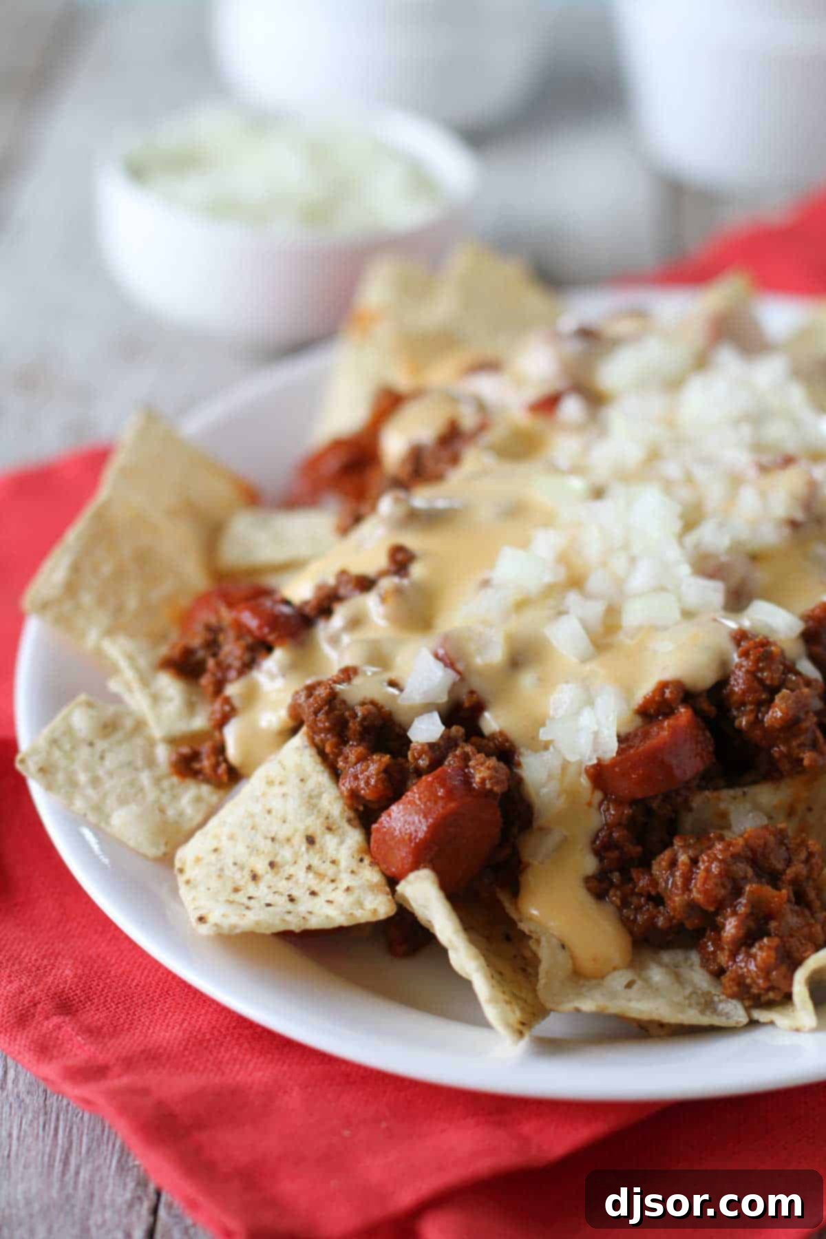 A large platter of Chili Dog Nachos, generously topped with savory chili, hot dogs, and a creamy cheese sauce, garnished with fresh minced onions.