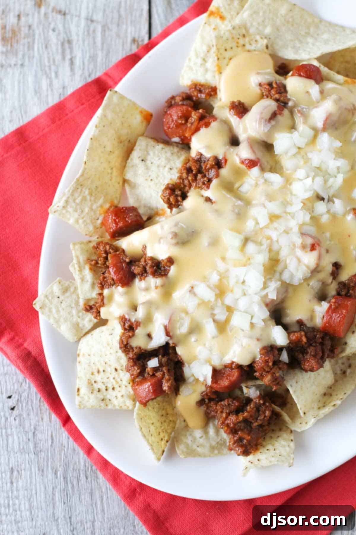 A close-up shot of a plate brimming with freshly made Chili Dog Nachos, featuring golden tortilla chips, hearty chili, and gooey melted cheese.