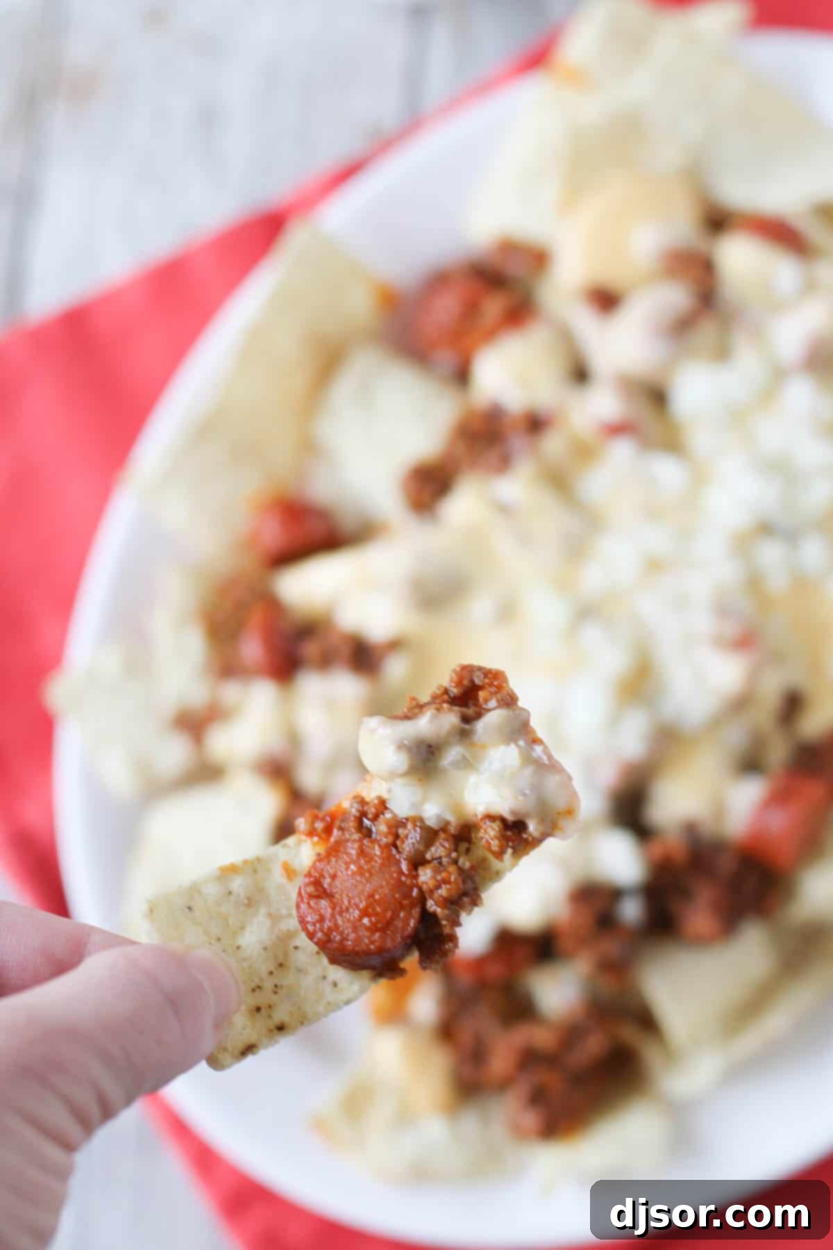 A hand reaching in to scoop a generous serving of Chili Dog Nachos from a large platter, showcasing the rich chili and melted cheese.