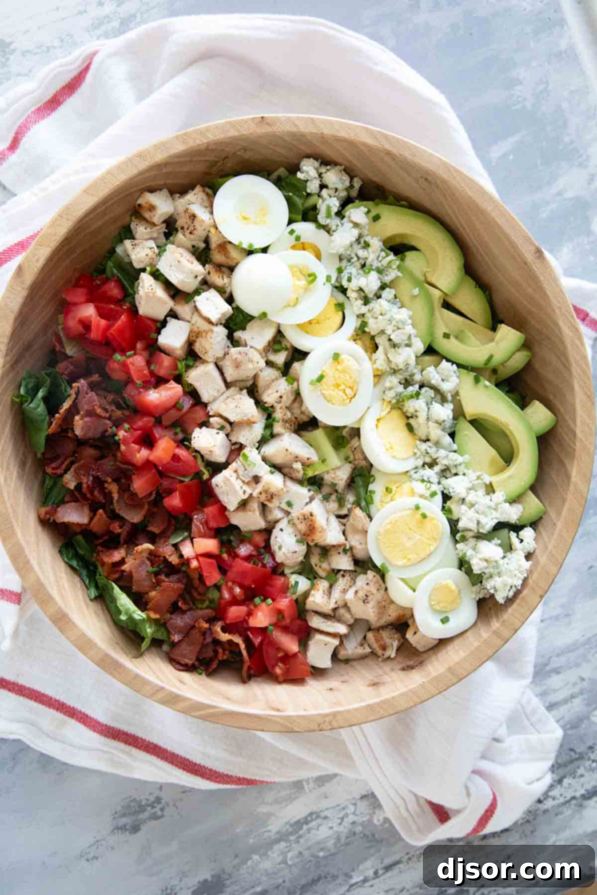 Cobb Salad with toppings arranged in lines on top in a large bowl.