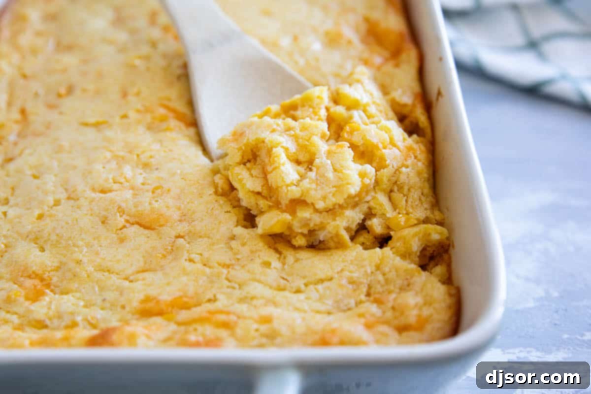Casserole dish of corn casserole with a wooden spoon dishing some out.