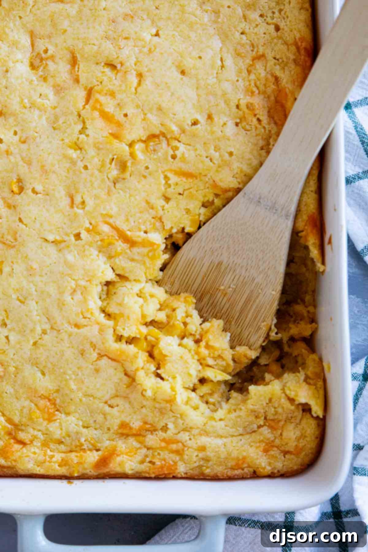Dish of corn casserole with a wooden spoon.