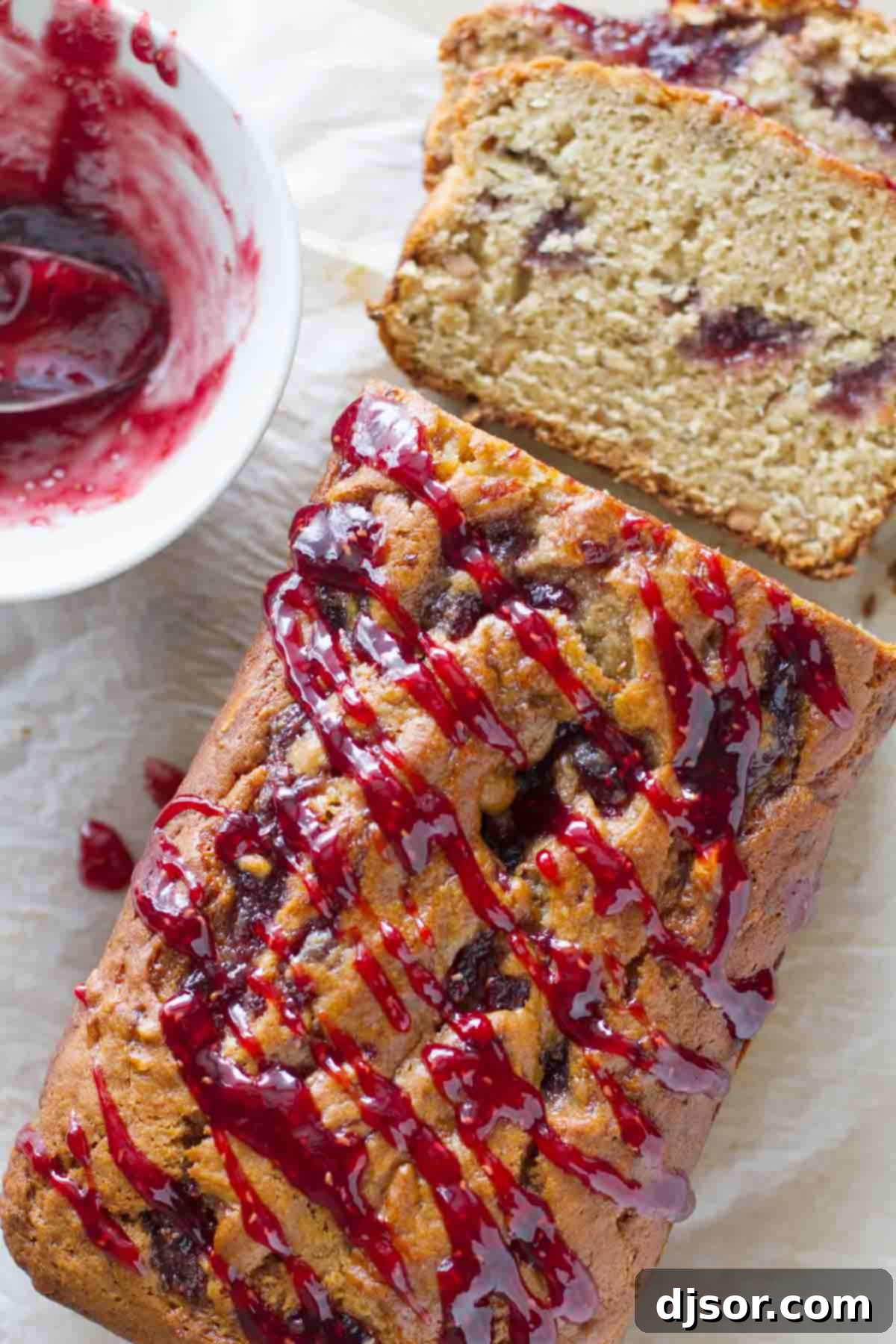 Peanut Butter Jelly Swirl Banana Bread 2 A beautifully baked loaf of Peanut Butter and Jelly Banana Bread, showcasing a vibrant raspberry jam drizzle on top and hints of the jam swirl within its golden-brown crust.