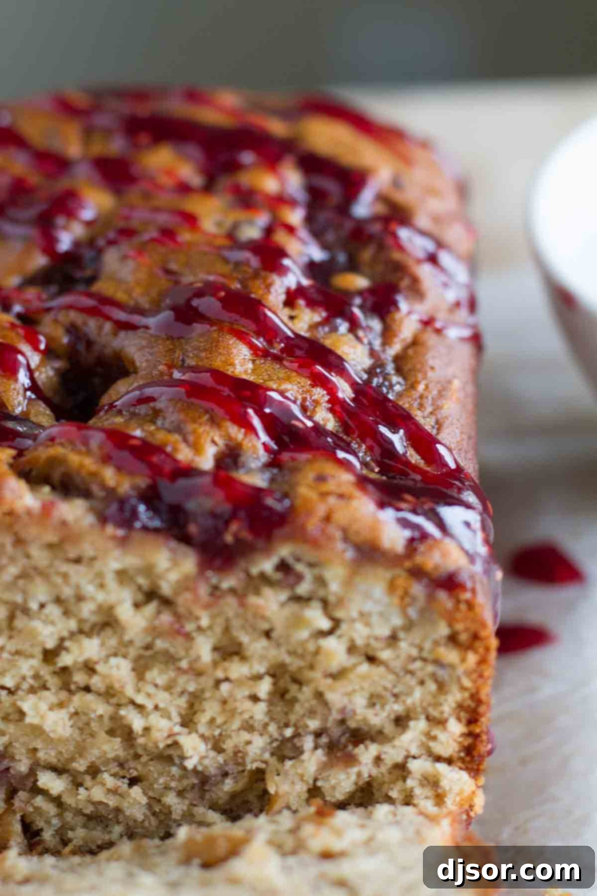 Peanut Butter Jelly Swirl Banana Bread 3 A close-up shot of a freshly baked Peanut Butter and Jelly Banana Bread loaf, highlighting the luscious raspberry jam swirl on its surface.