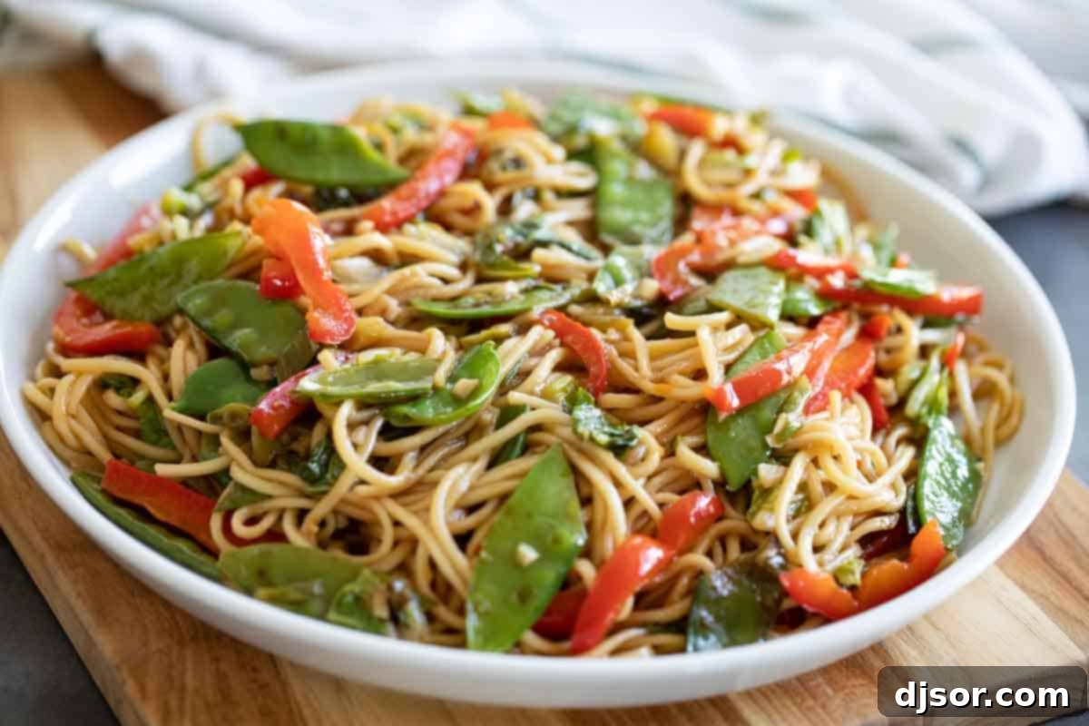 A steaming bowl of homemade Lo Mein noodles, brimming with colorful vegetables like snow peas, Napa cabbage, and red bell peppers.