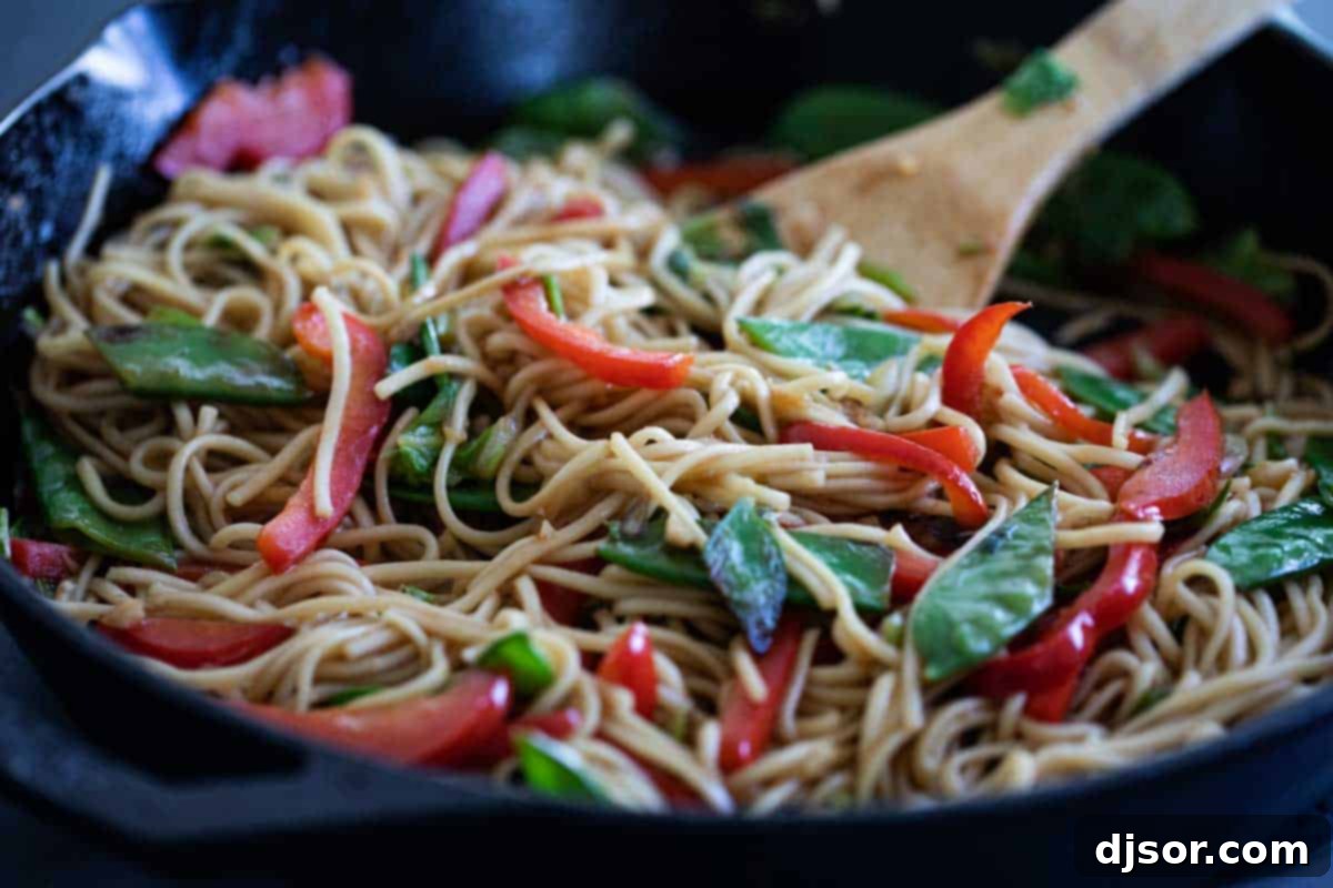 A large skillet filled with vibrant Chinese noodles and stir-fried vegetables, coated in a savory sauce.