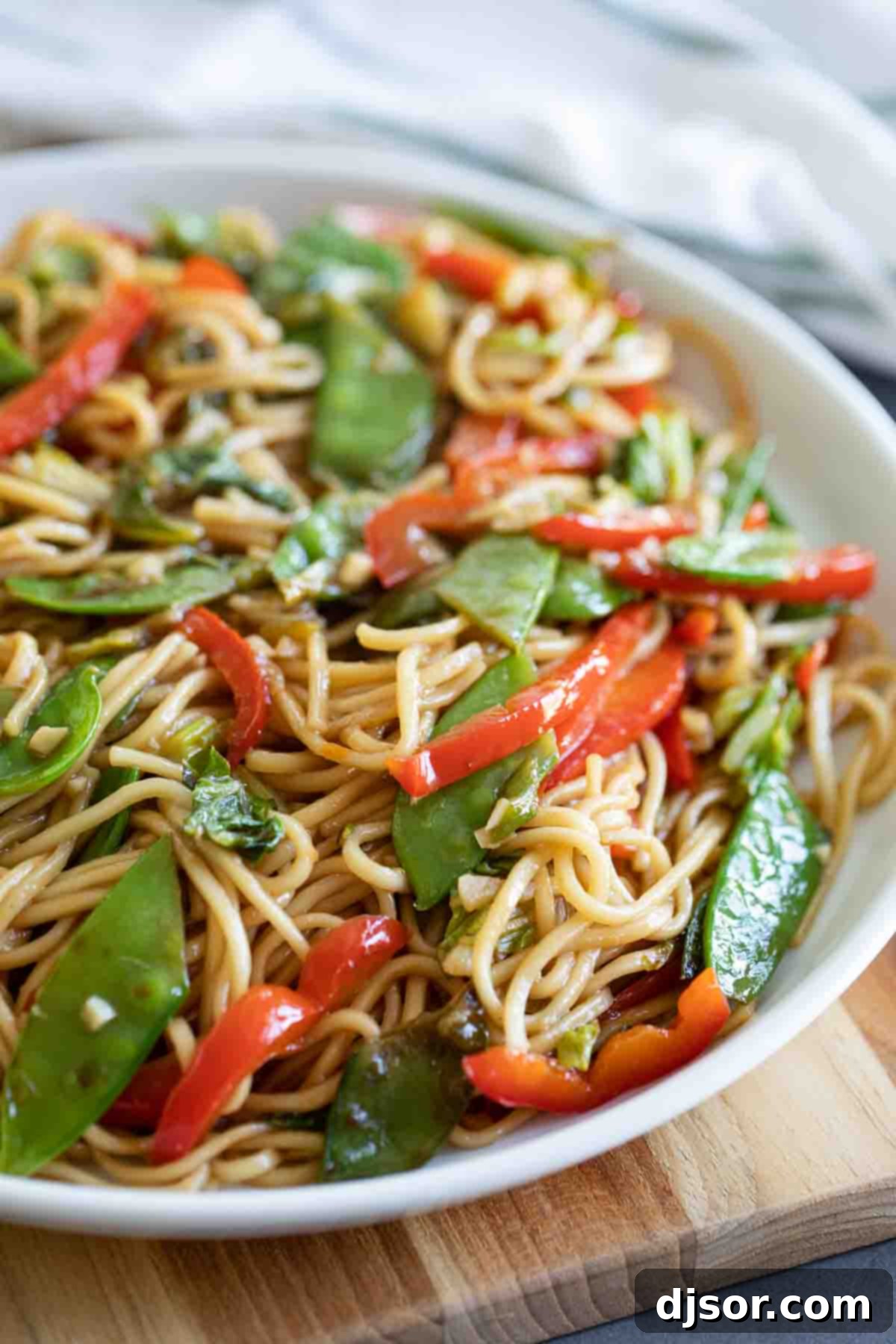 A serving dish of Lo Mein noodles with a colorful mix of cabbage, snow peas, and red bell peppers, ready to be enjoyed.