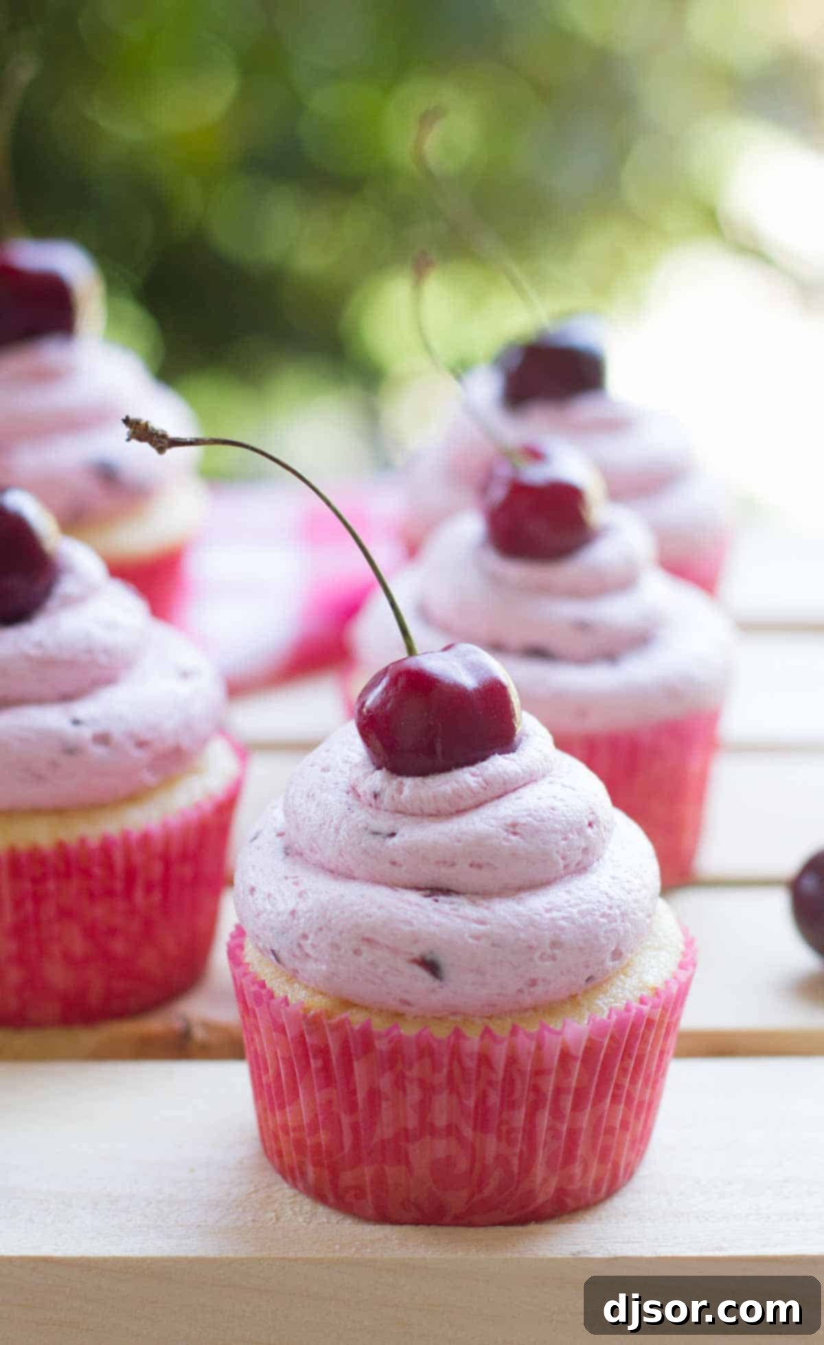 Almond cupcakes topped with fresh cherry frosting with a fresh cherry on top, elegantly presented.