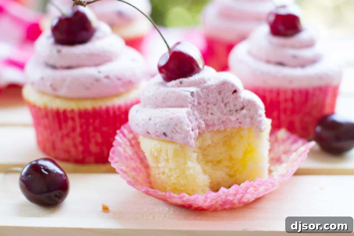 A freshly baked almond cupcake with a bite taken out of it, revealing its moist texture and topped with cherry frosting.