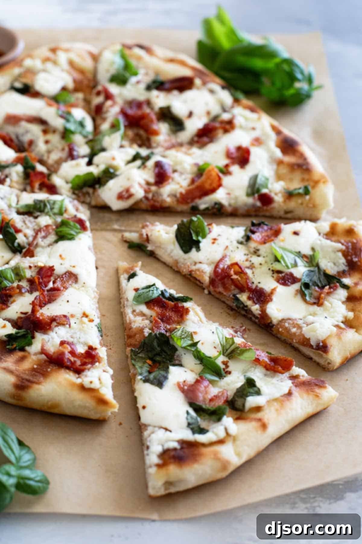 Fire-Kissed Bacon & Basil Bianca Pizza 2 Slices of Grilled White Pizza with Bacon and Basil with more fresh basil on the side, ready to be served.