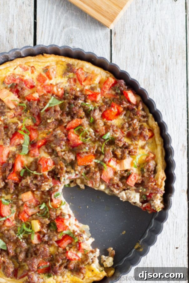 A slice of Savory Italian Tart on a white plate, revealing the perfectly baked puff pastry crust and the vibrant filling of sausage, tomatoes, and cheese.