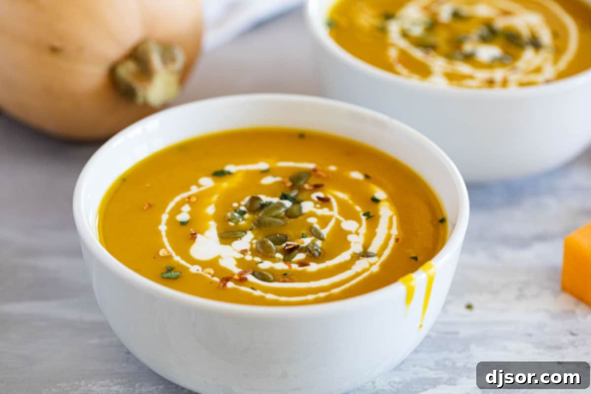 Two vibrant bowls of Curried Butternut Squash Soup, garnished with a swirl of cream and a sprinkle of crunchy pepitas.