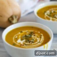 A single elegant bowl of Curried Butternut Squash Soup, garnished with a creamy swirl and a scattering of pepitas, ready to be savored.