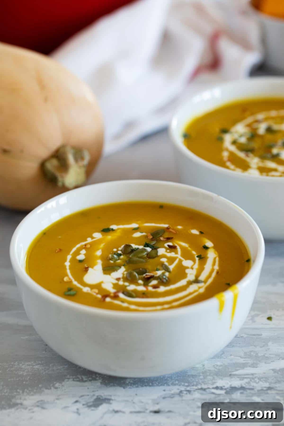 A single elegant bowl of Curried Butternut Squash Soup, garnished with a creamy swirl and a scattering of pepitas, ready to be savored.