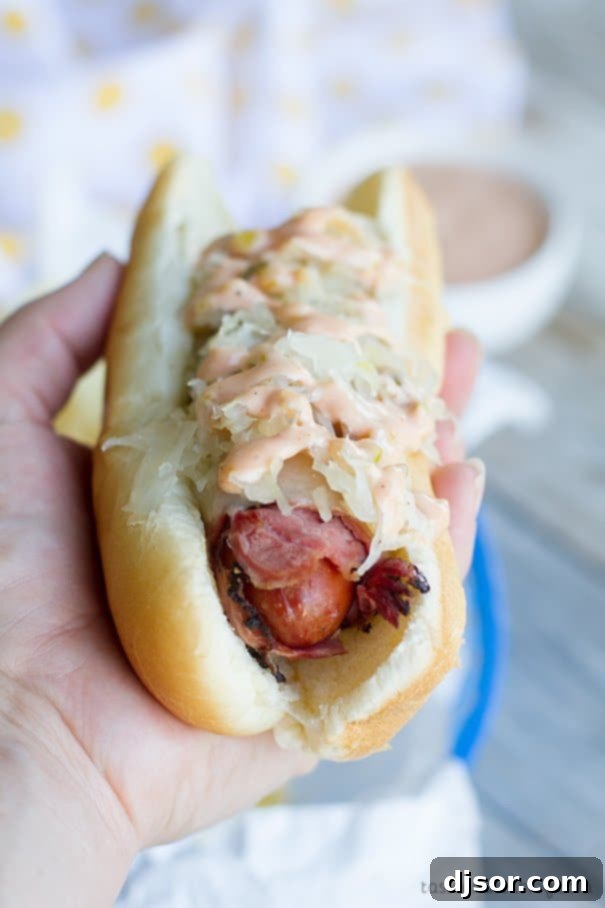 Enjoying a Pastrami Wrapped Hot Dog Hand holding a delicious Pastrami Wrapped Hot Dog ready to be eaten.