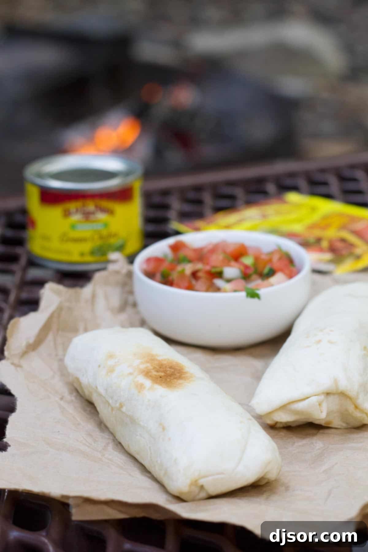Three foil-wrapped breakfast burritos placed directly in the hot coals of a campfire, ready to heat.