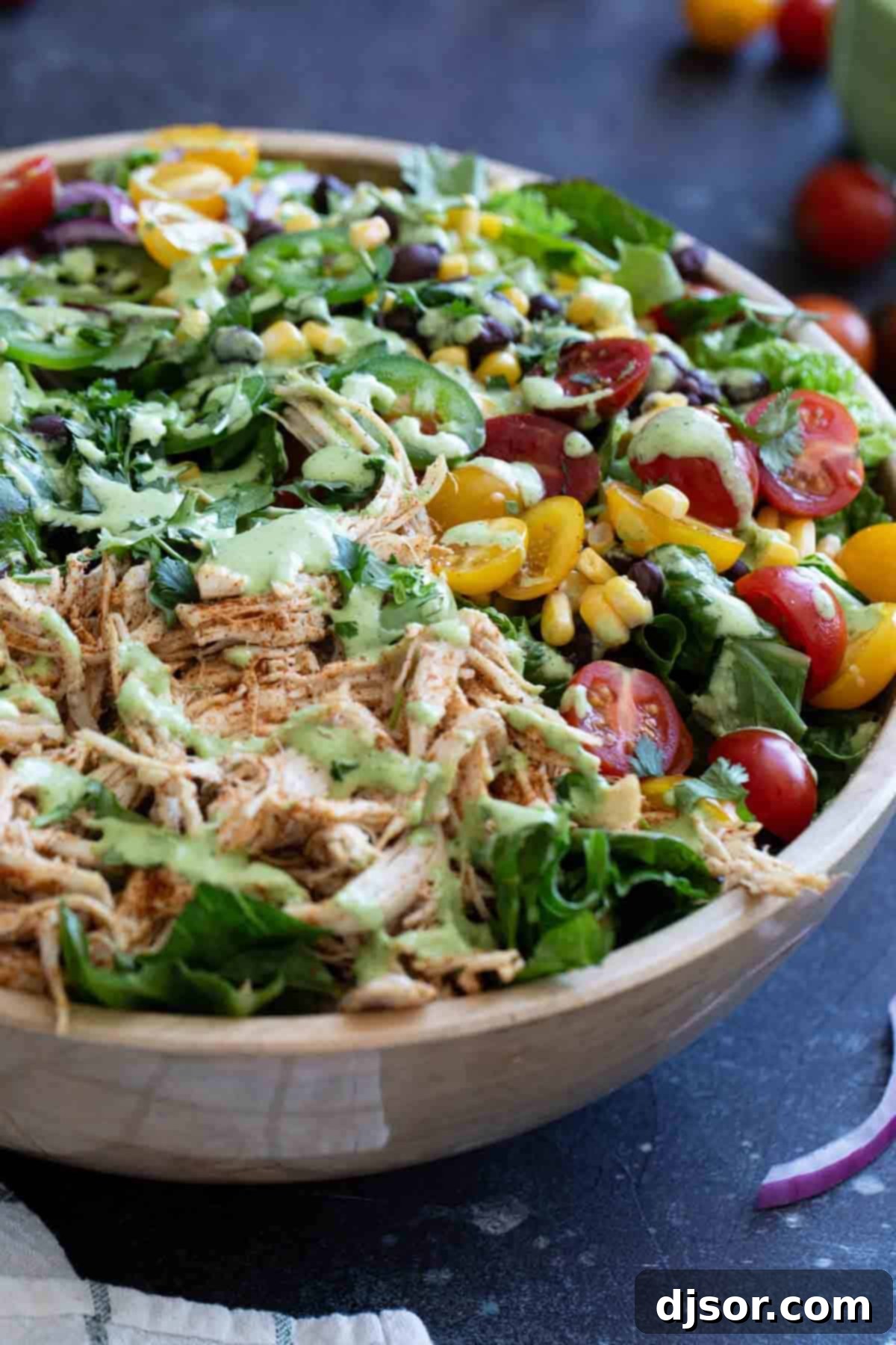 Southwest chicken salad in a wooden bowl, topped with spicy cilantro dressing.