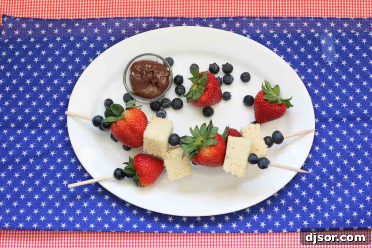 Two festive 4th of July Dessert Kabobs, featuring cubed pound cake, fresh blueberries, and bright red strawberries, arranged artfully for a patriotic treat.