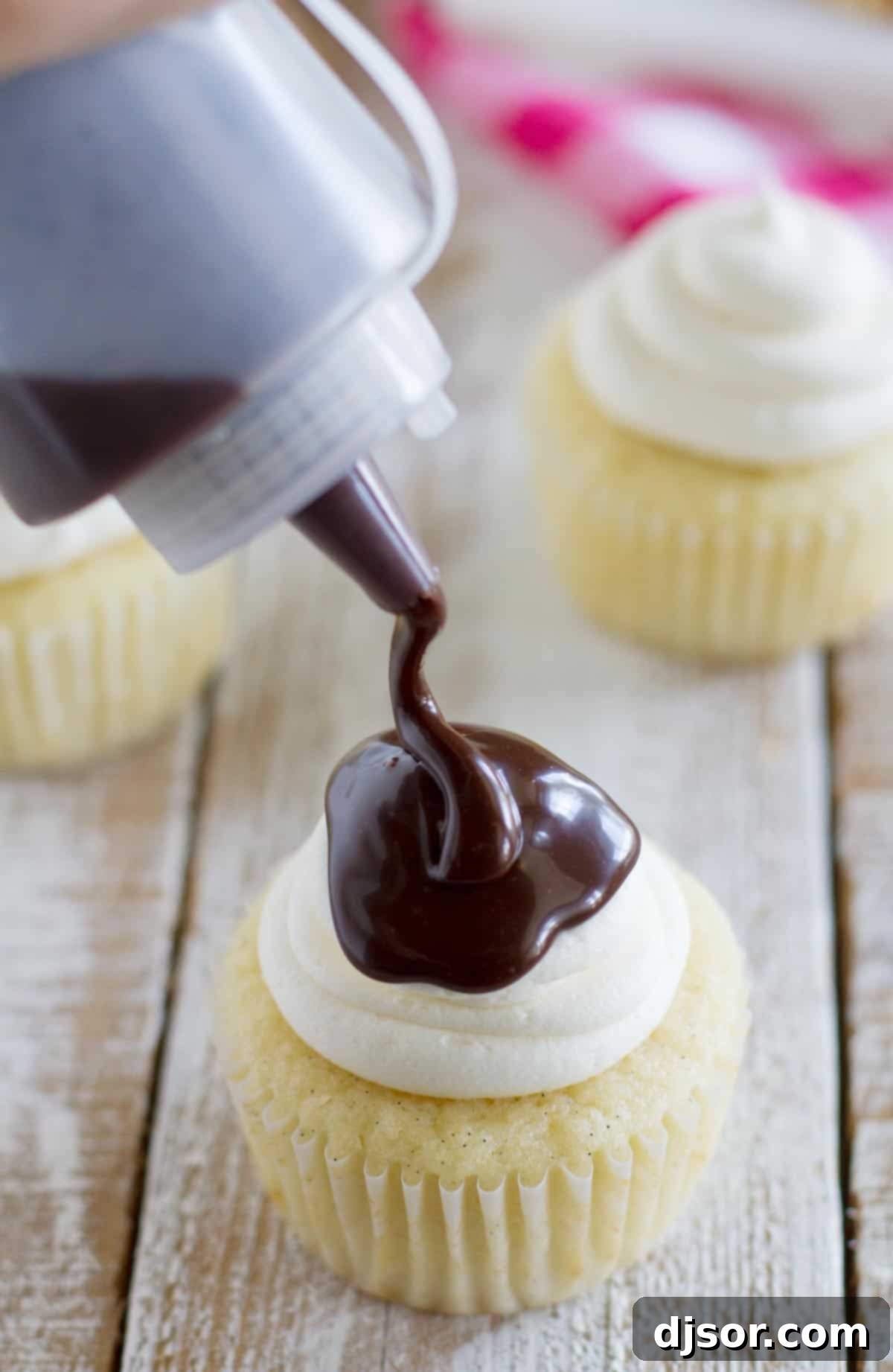 Hand drizzling chocolate sauce over a Drumstick Cupcake, creating a delicious shell effect.
