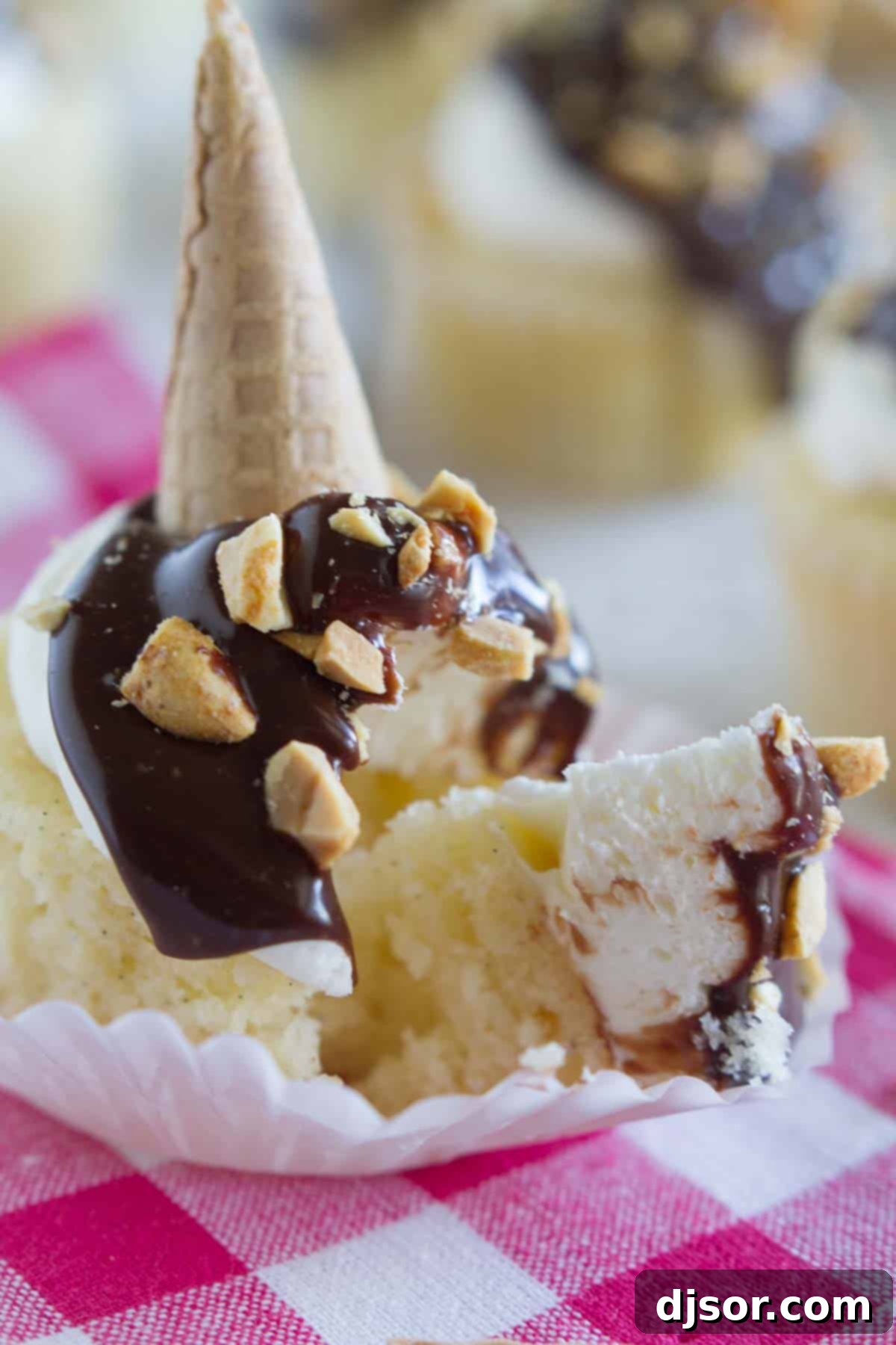 A Drumstick Cupcake with a bite taken out, showcasing the layers of vanilla cake, buttercream, chocolate, and peanuts.
