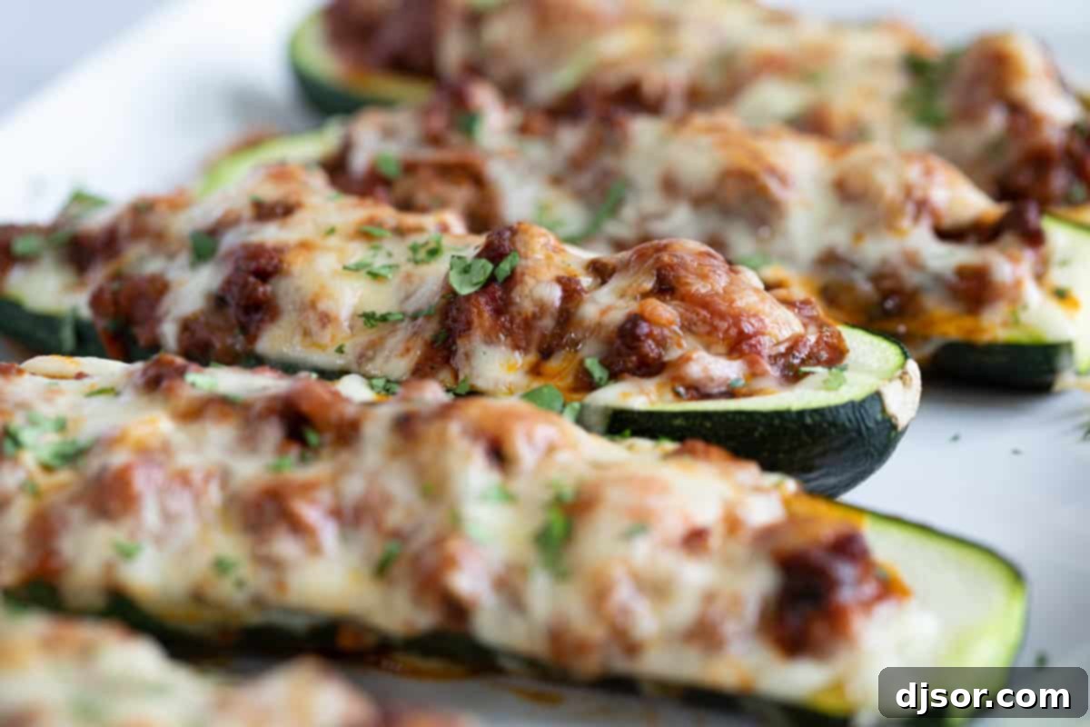 Close-up of golden-brown Stuffed Zucchini Boats, brimming with a savory mixture of beef, Italian sausage, and marinara sauce, topped with bubbly melted mozzarella cheese and fresh parsley.