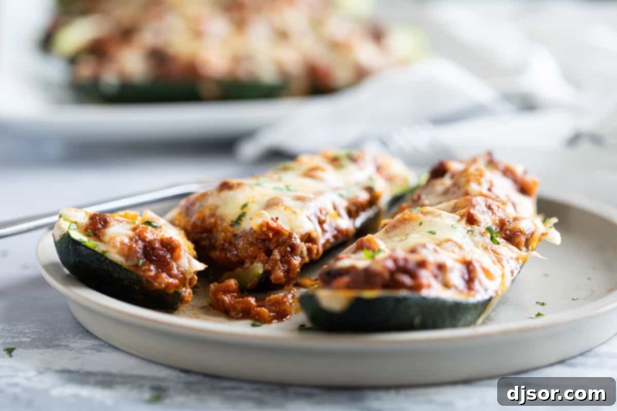 Stuffed Zucchini Boats on a plate, with one boat cut in half to show the hearty meat and cheese filling inside.