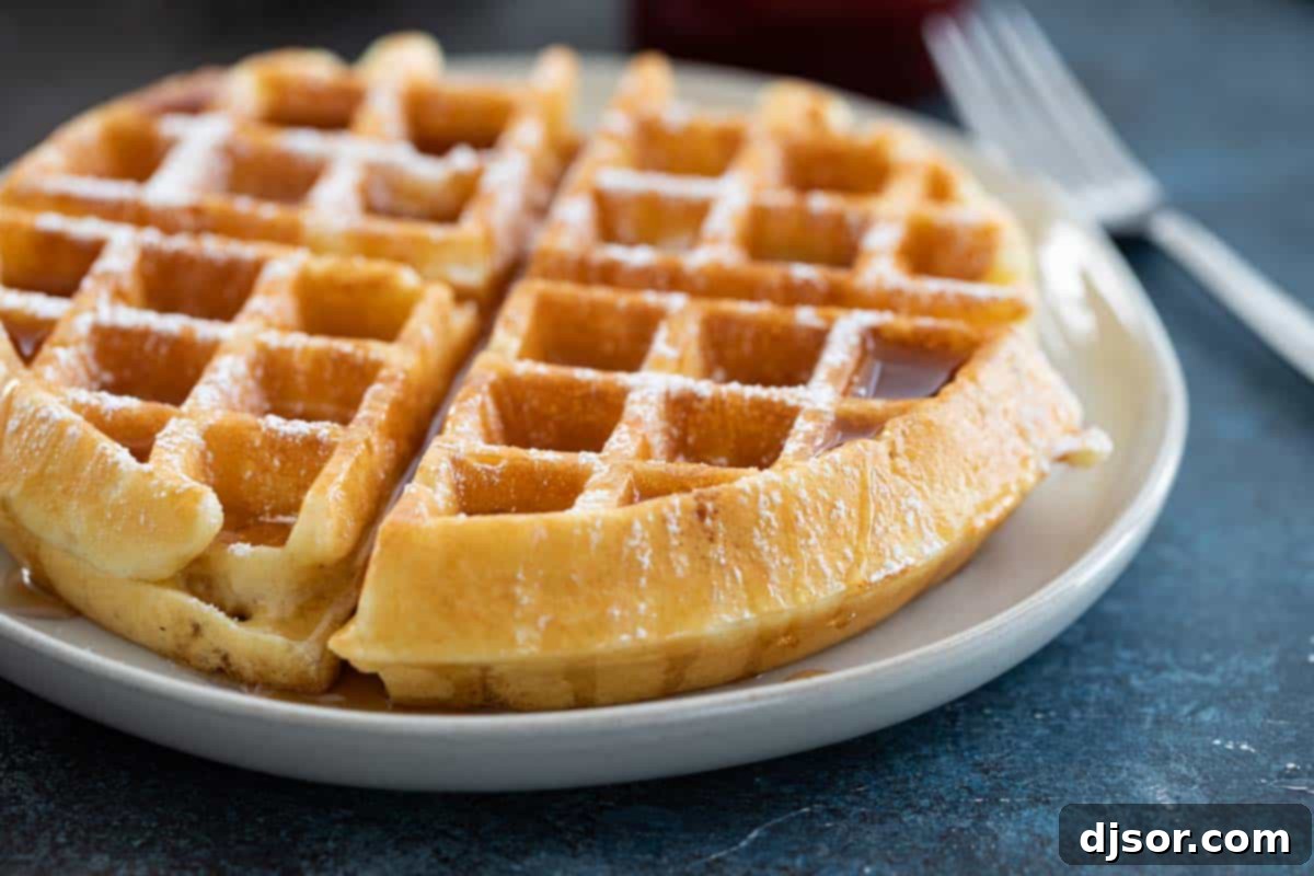 Golden-brown waffle on a plate, drizzled with maple syrup and sprinkled with powdered sugar, ready for breakfast.