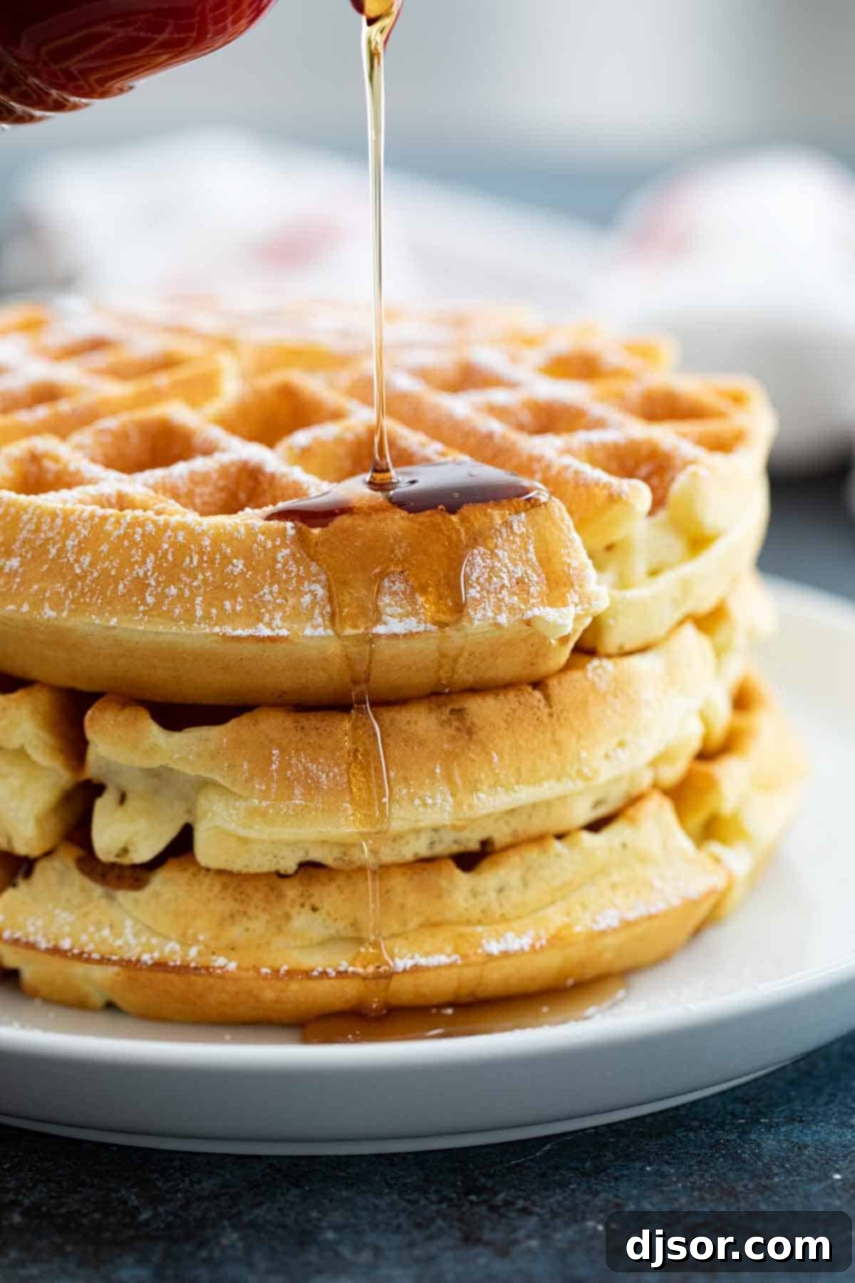Rich maple syrup pouring generously over a stack of golden-brown homemade waffles, creating an irresistible breakfast scene.
