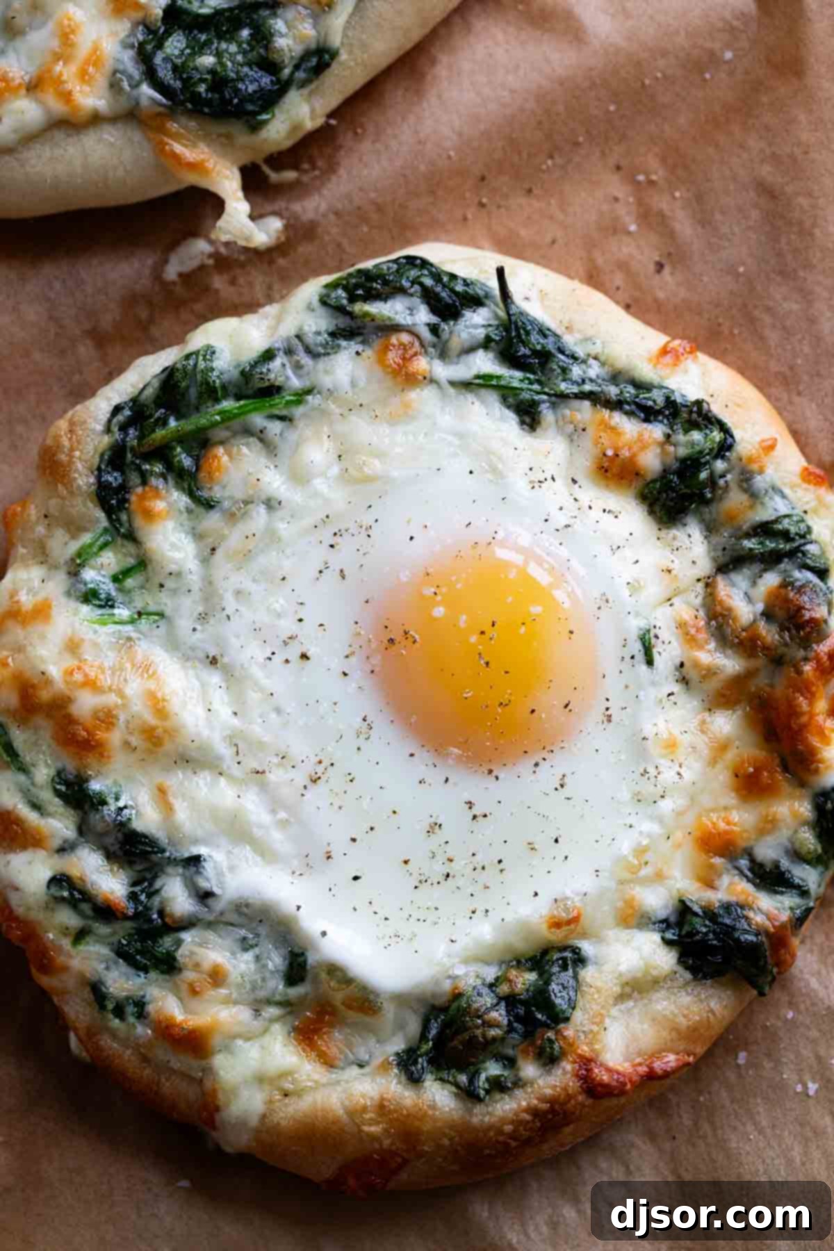 Breakfast meets dinner with this Egg Pizza with Creamed Spinach which tops pizza dough with creamed spinach and a perfectly cooked egg. A baked individual egg pizza with creamed spinach and melted mozzarella, showing a perfectly set egg yolk.