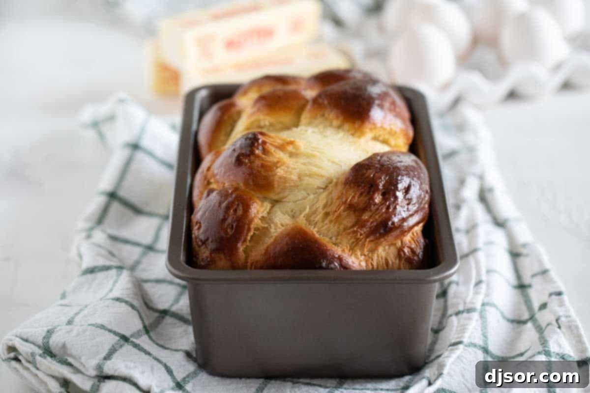 A perfectly baked, golden brown brioche loaf still warm in its loaf pan, showcasing a beautiful, glossy crust.
