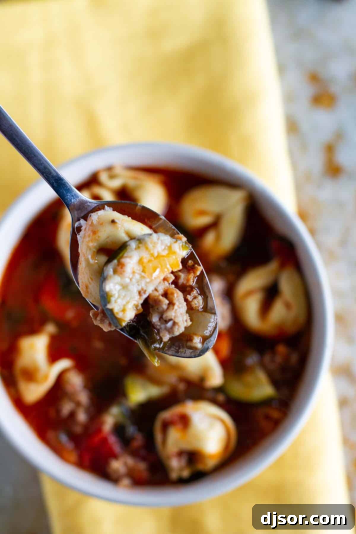 A spoonful of Sausage Tortellini Soup being lifted from a bowl, showcasing the sausage, tortellini, and colorful vegetables.