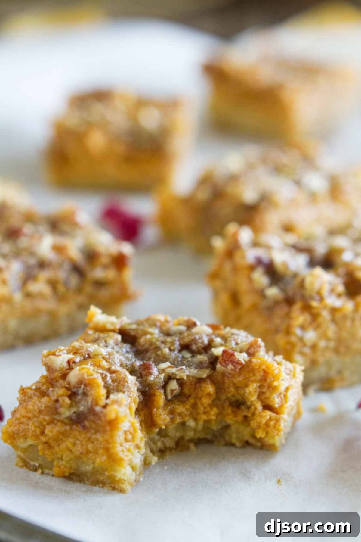 A close-up view of a Pumpkin Pie Bar with a bite taken, revealing the rich, creamy pumpkin filling and the textured oat crust beneath the sweet pecan topping.