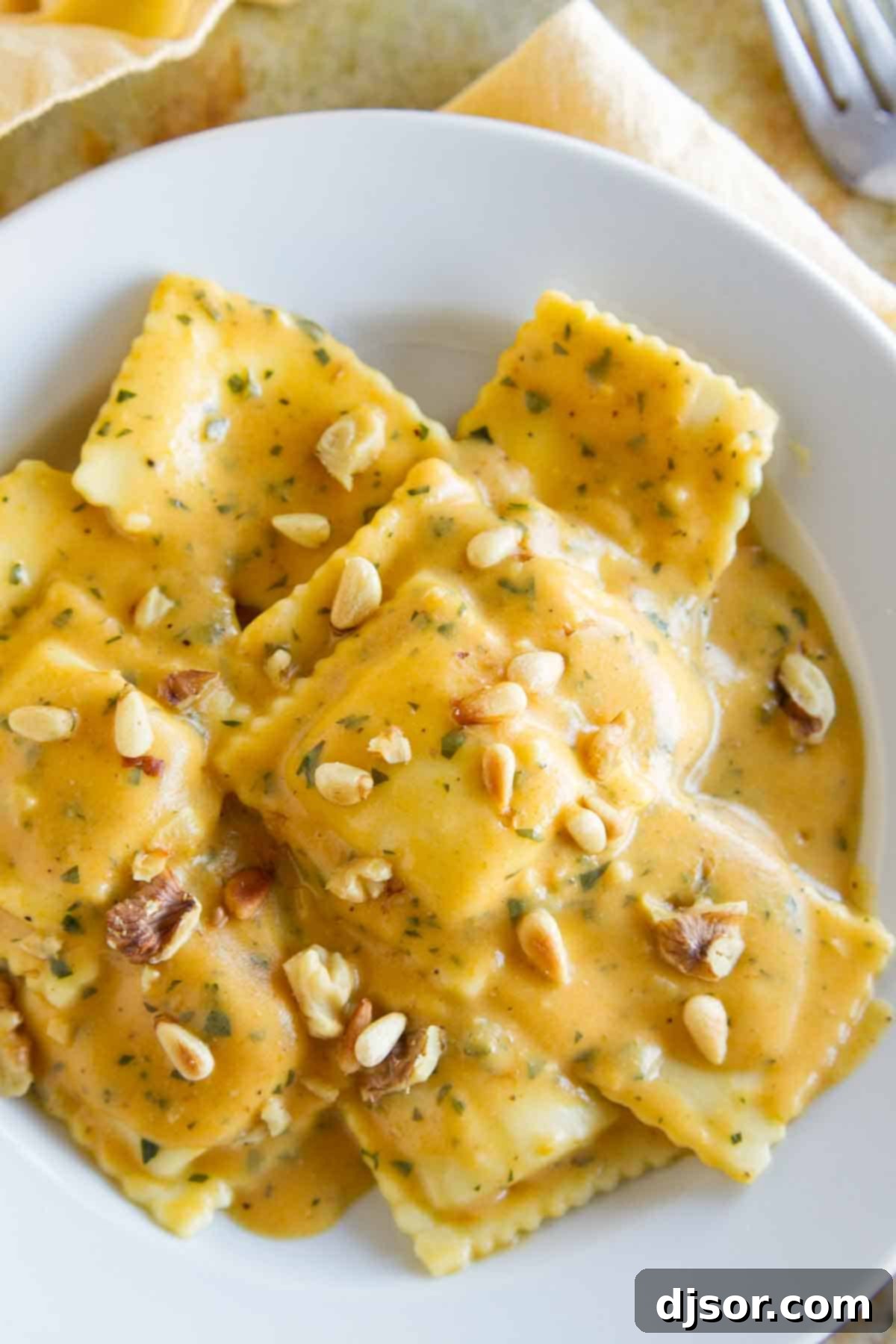 Creamy Pumpkin Ravioli: A Family Favorite Overhead view of a comforting bowl of ravioli with pumpkin pasta sauce, beautifully garnished with toasted pine nuts and walnuts, ready to be enjoyed.