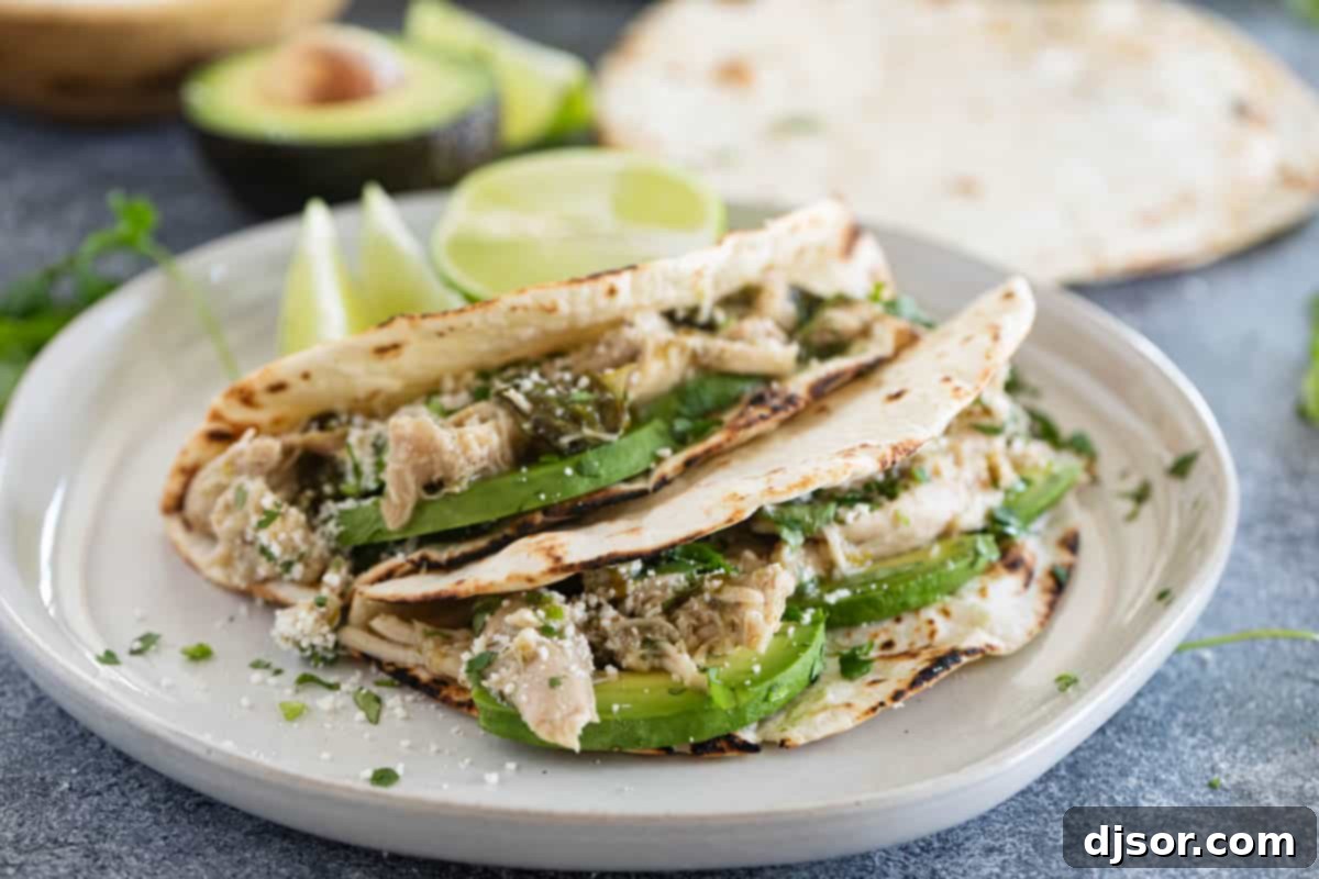 Two Slow Cooker Chicken Tacos on flour tortillas on a plate, garnished with fresh cilantro and avocado slices.