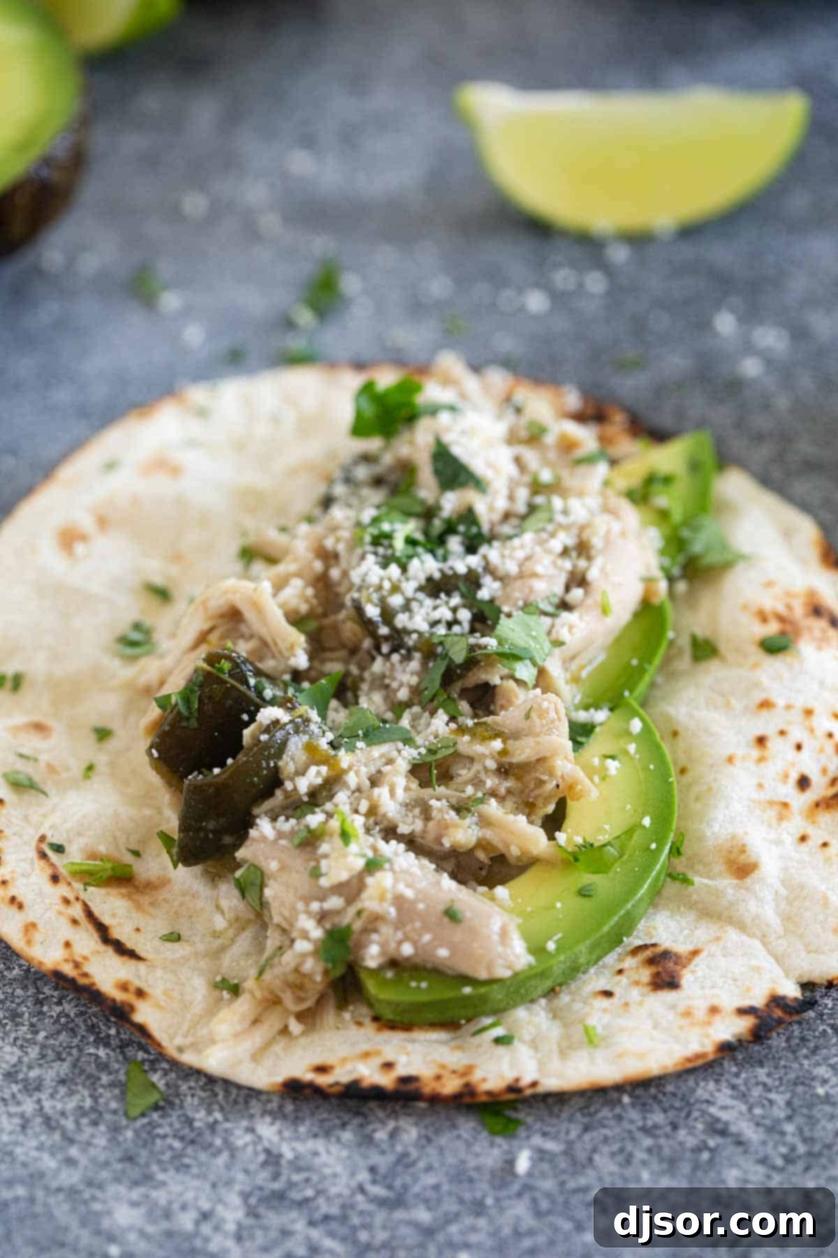 An open taco filled with slow cooker chicken, sliced avocado, cotija cheese, and fresh cilantro, ready to be eaten.