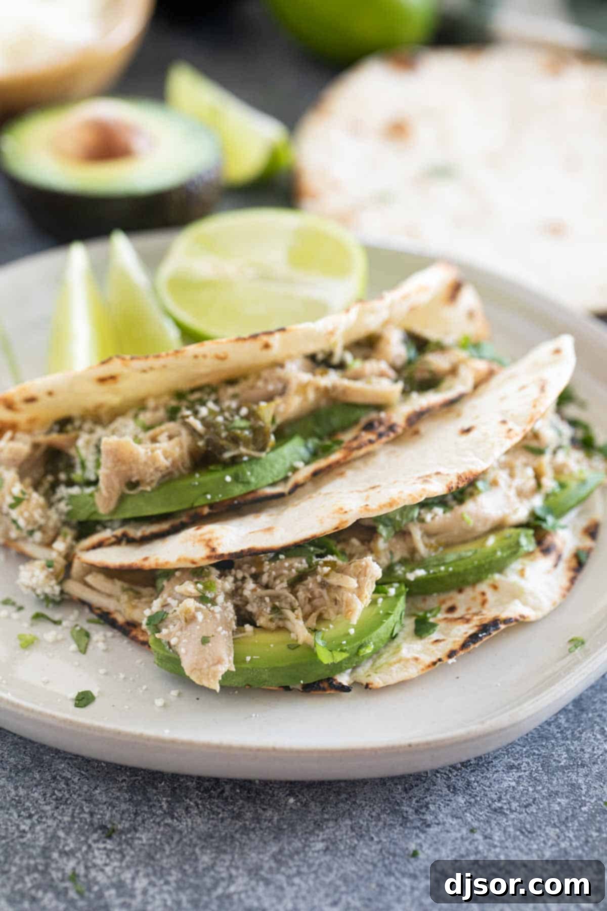 Slow Cooker Chicken Tacos with avocado and cilantro on a plate, highlighting the fresh toppings.