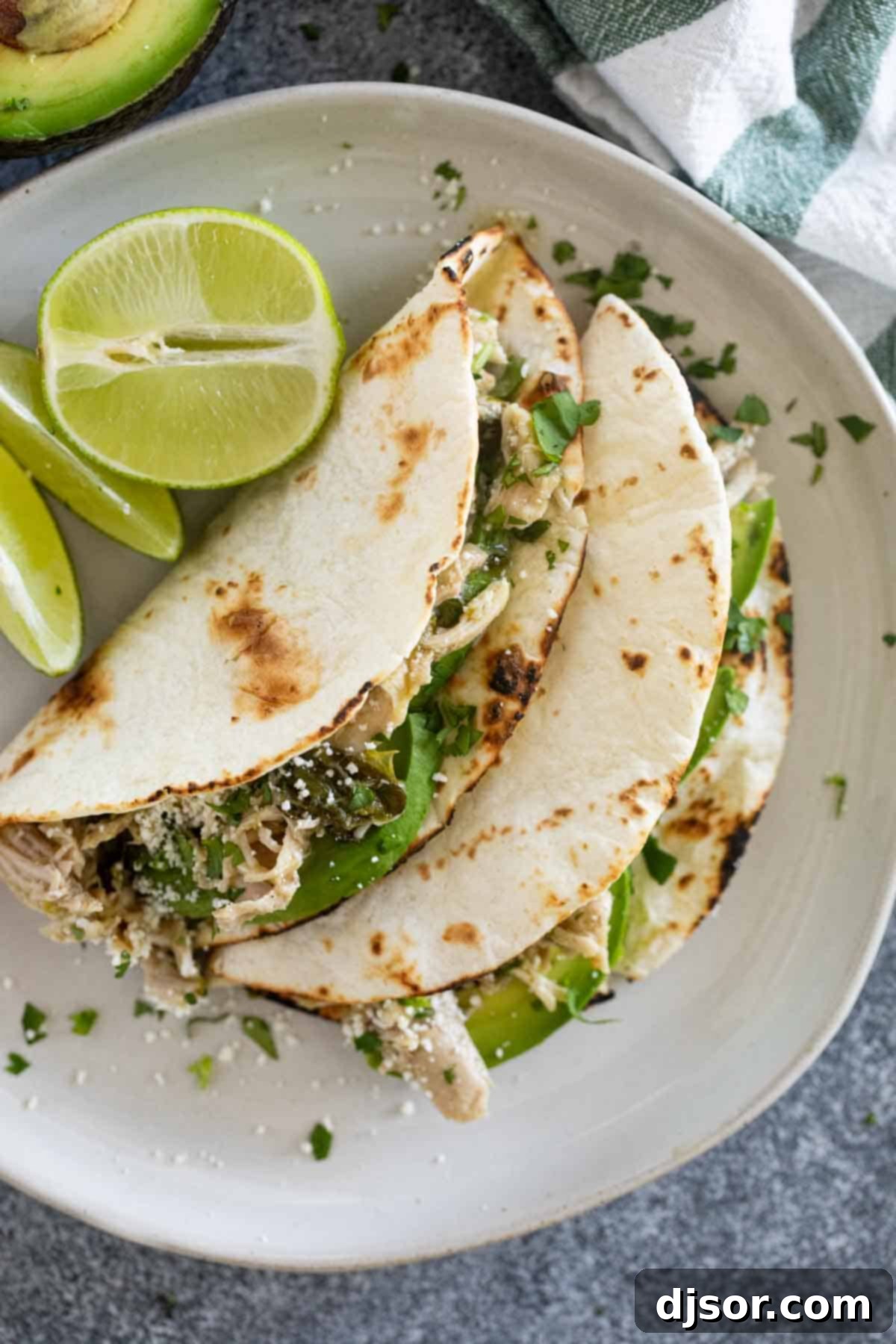 Two slow cooker chicken tacos with charred tortillas, garnished with cilantro and avocado.