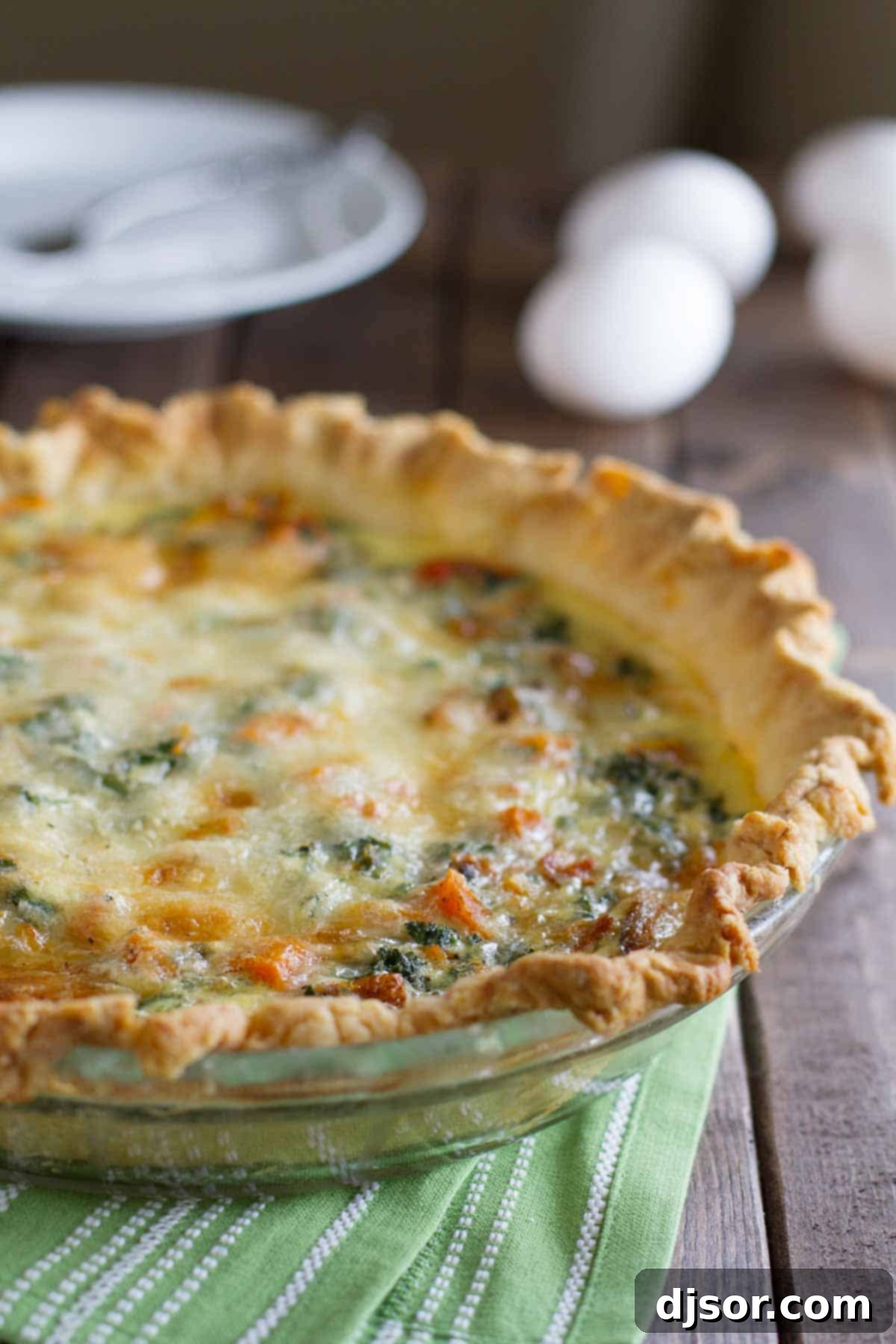 Golden brown Butternut Squash Quiche with Kale in a pie dish. A whole butternut squash quiche with kale, freshly baked to golden perfection in a ceramic pie dish, ready to be sliced and served.